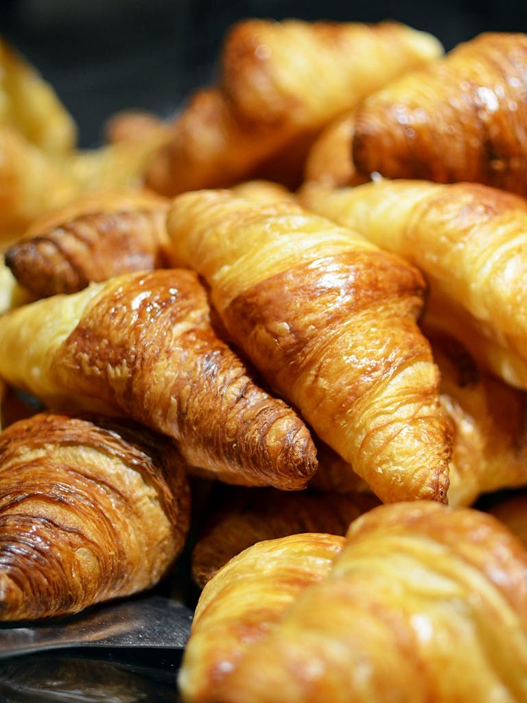 A stack of golden, freshly baked croissants showcasing flaky layers in a bakery setting.