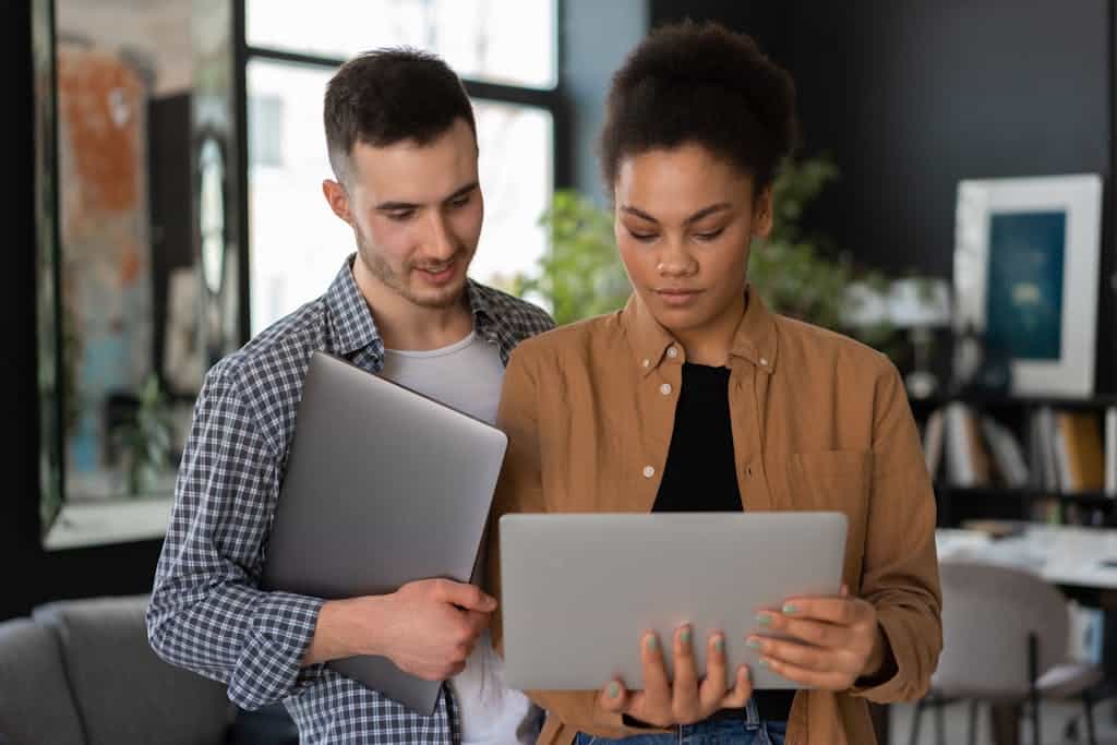 Two young adults collaborating with laptops in a stylish home office setting.